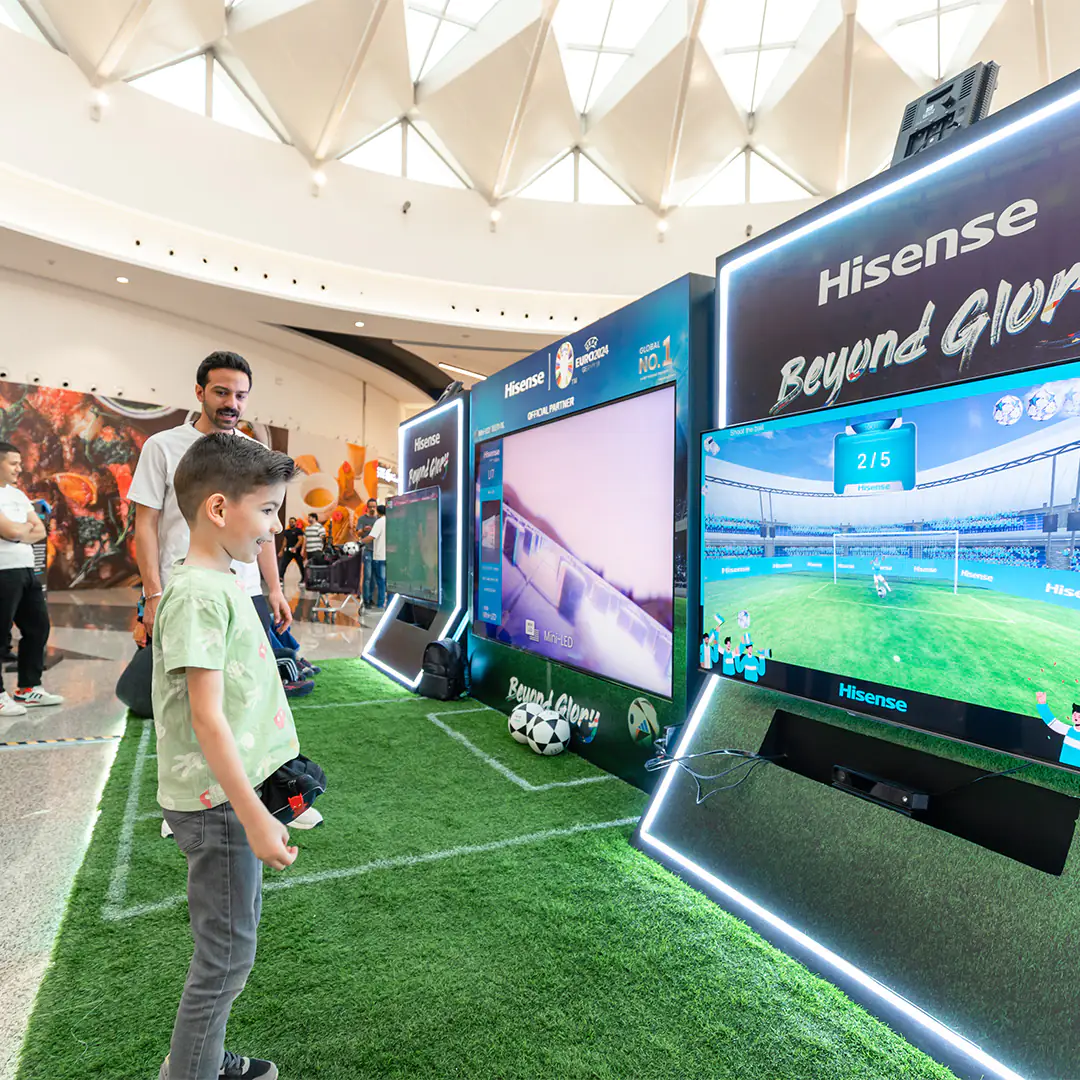 A child and his father interacting with a Hisense virtual football game display at a mall, promoting the brand's partnership with UEFA Euro 2024