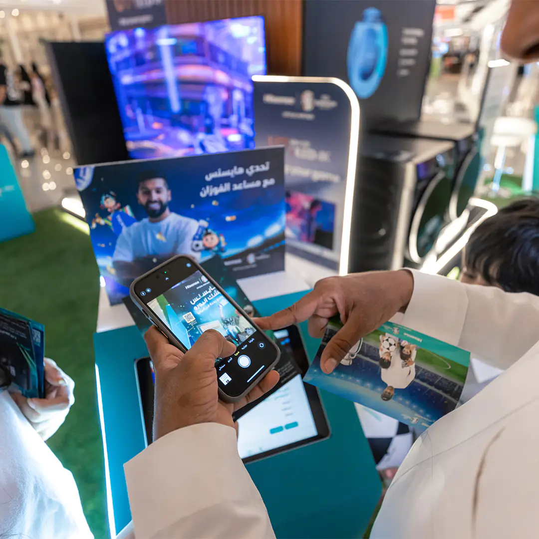 Person using a smartphone to scan Hisense promotional material at a mall event for the UEFA Euro 2024 partnership