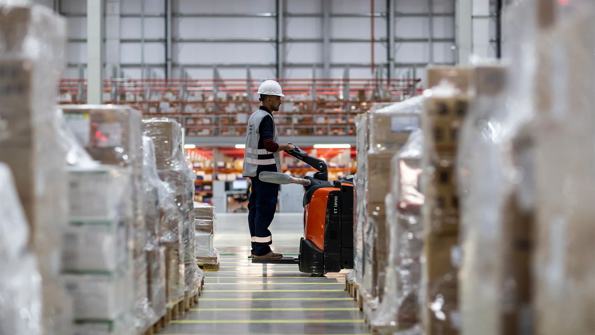 Warehouse worker operating a pallet truck at NUPCO warehouse, moving goods between storage areas for efficient distribution and logistics management