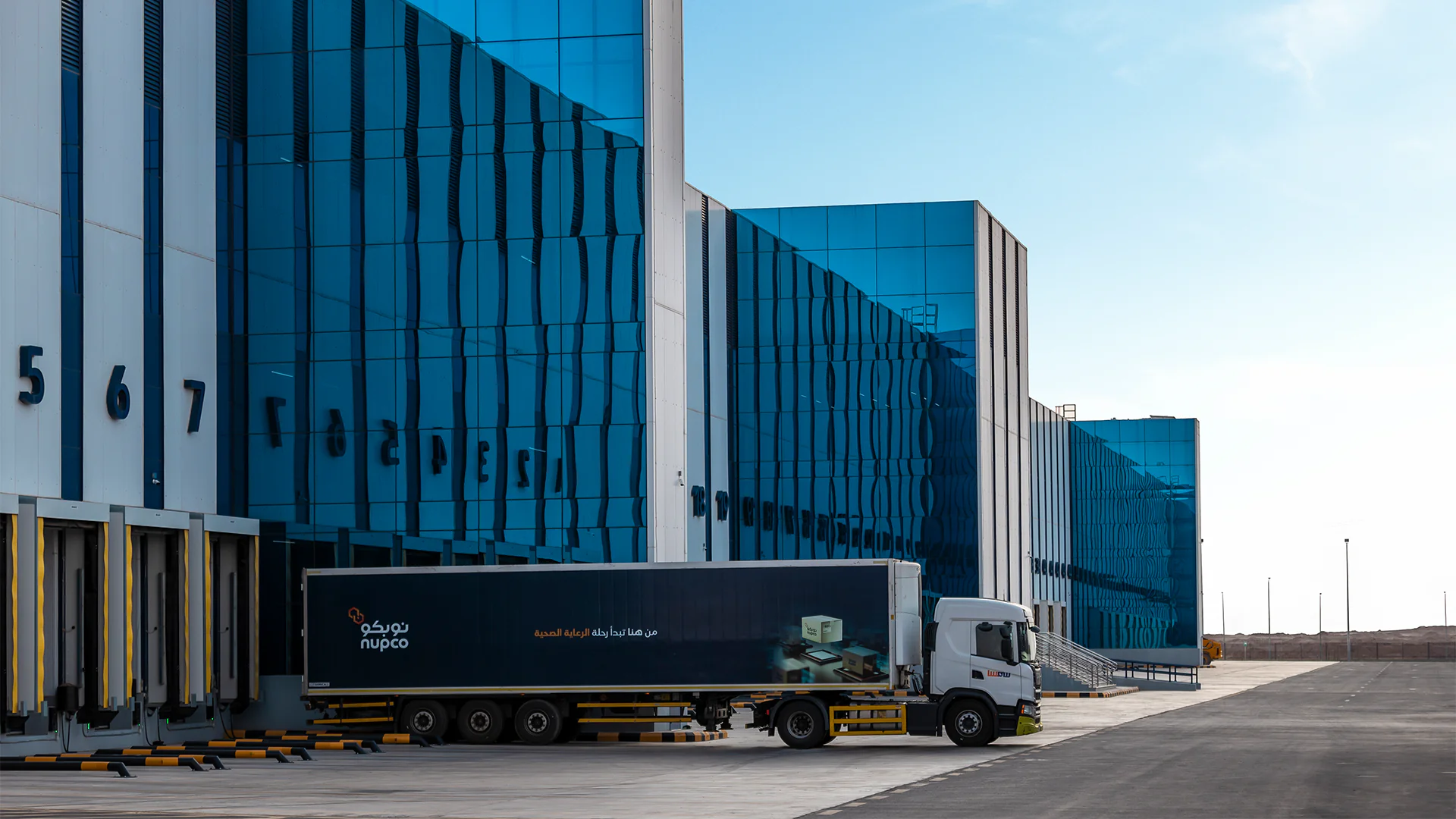 Exterior view of NUPCO's warehouse facility with a branded truck parked at the loading dock, ready for transportation