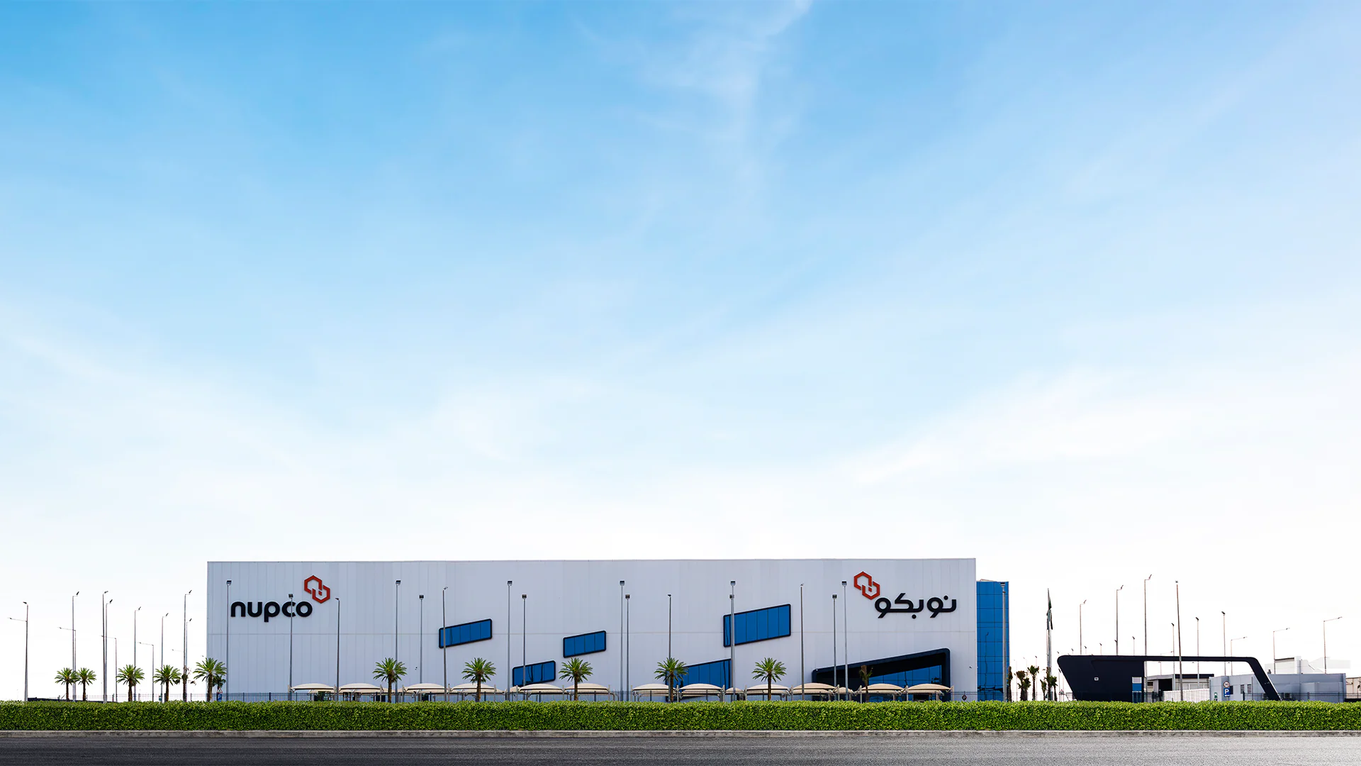 Wide exterior view of NUPCO's warehouse with the company logo, showcasing the modern architecture and clear sky background