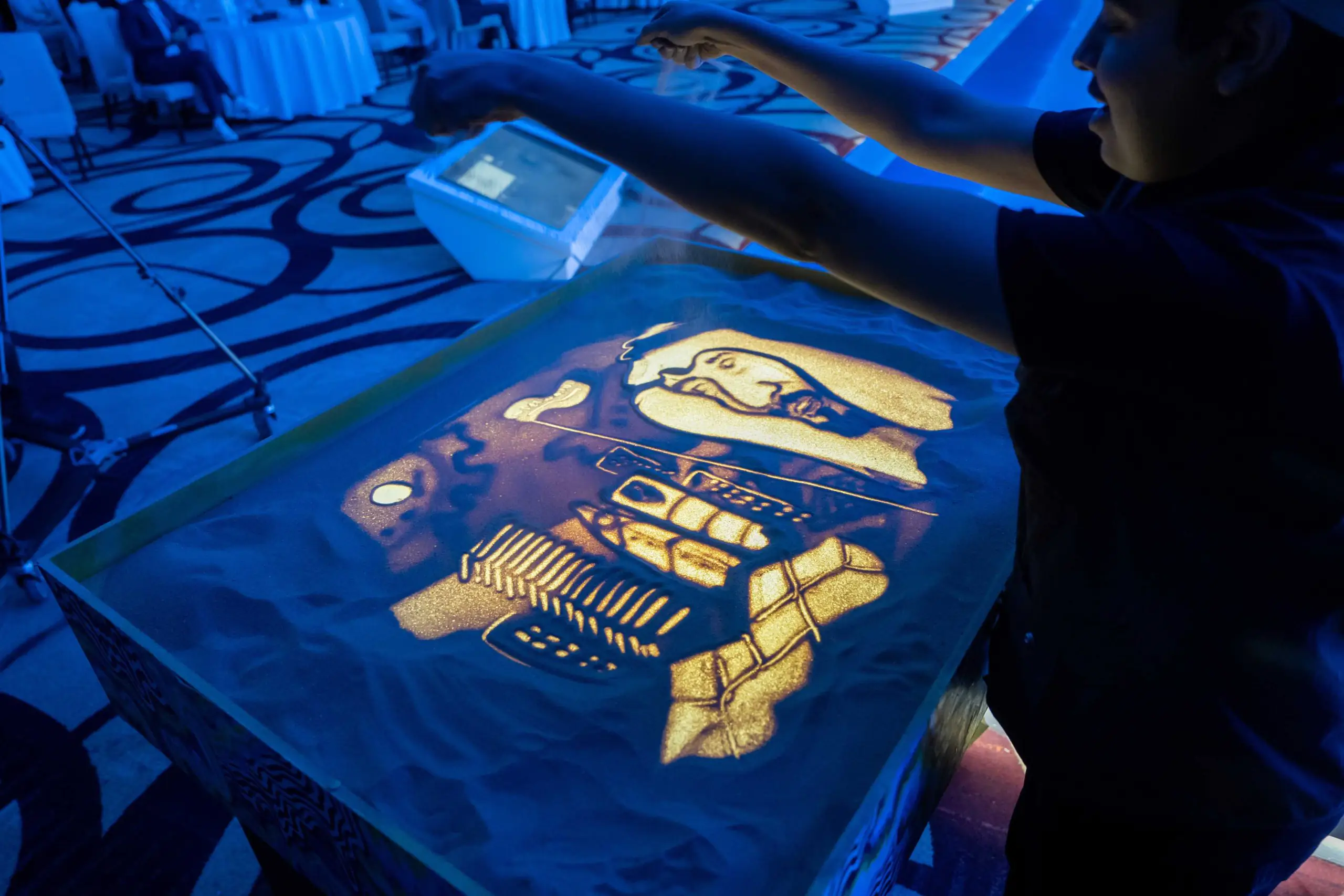 Sand art of King Salman, KSA flag, and Saudi towers with blue background.