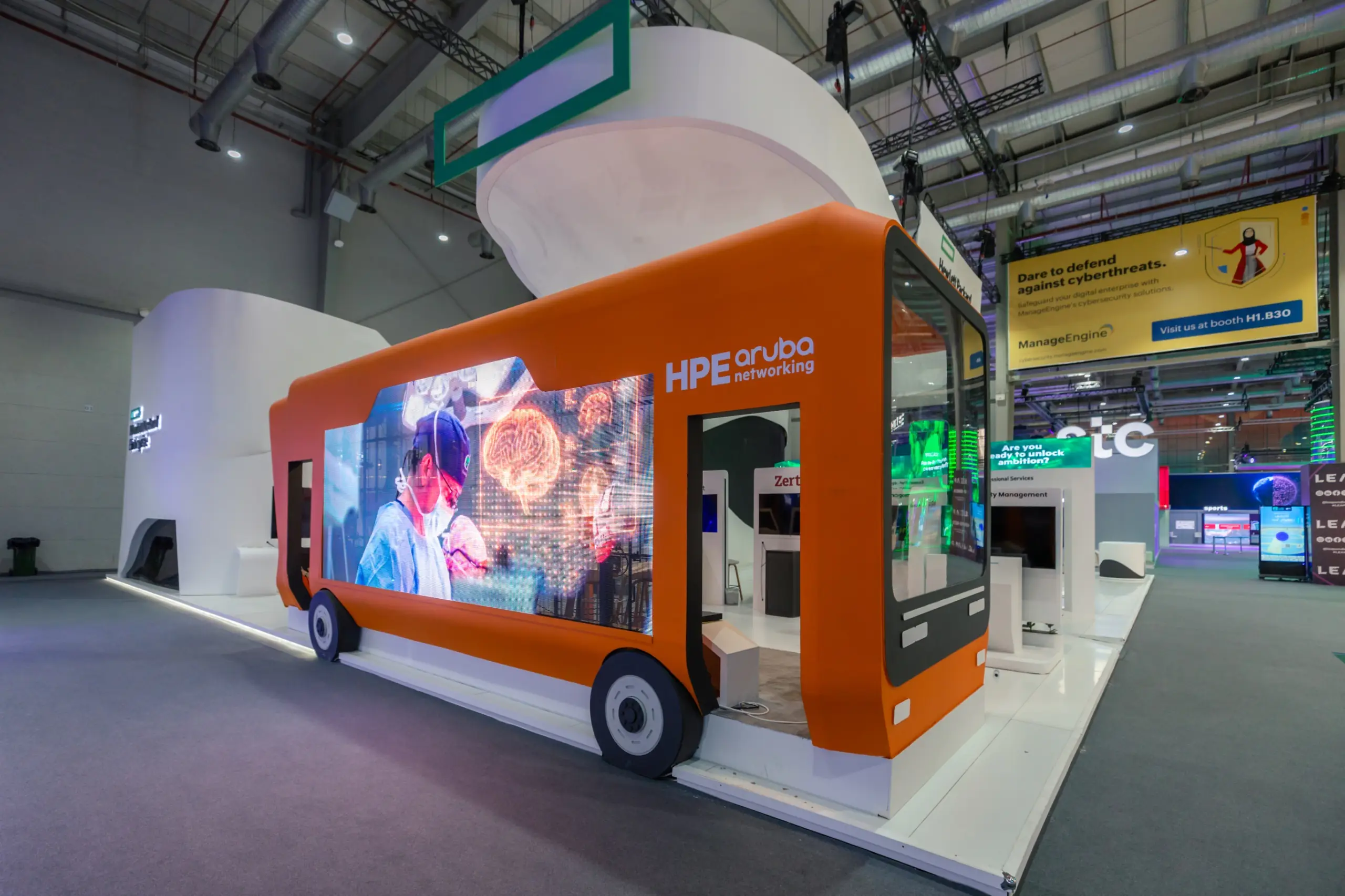 A trade show booth shaped like a bus with an LED screen displaying a medical scene, branded with HPE Aruba Networking.