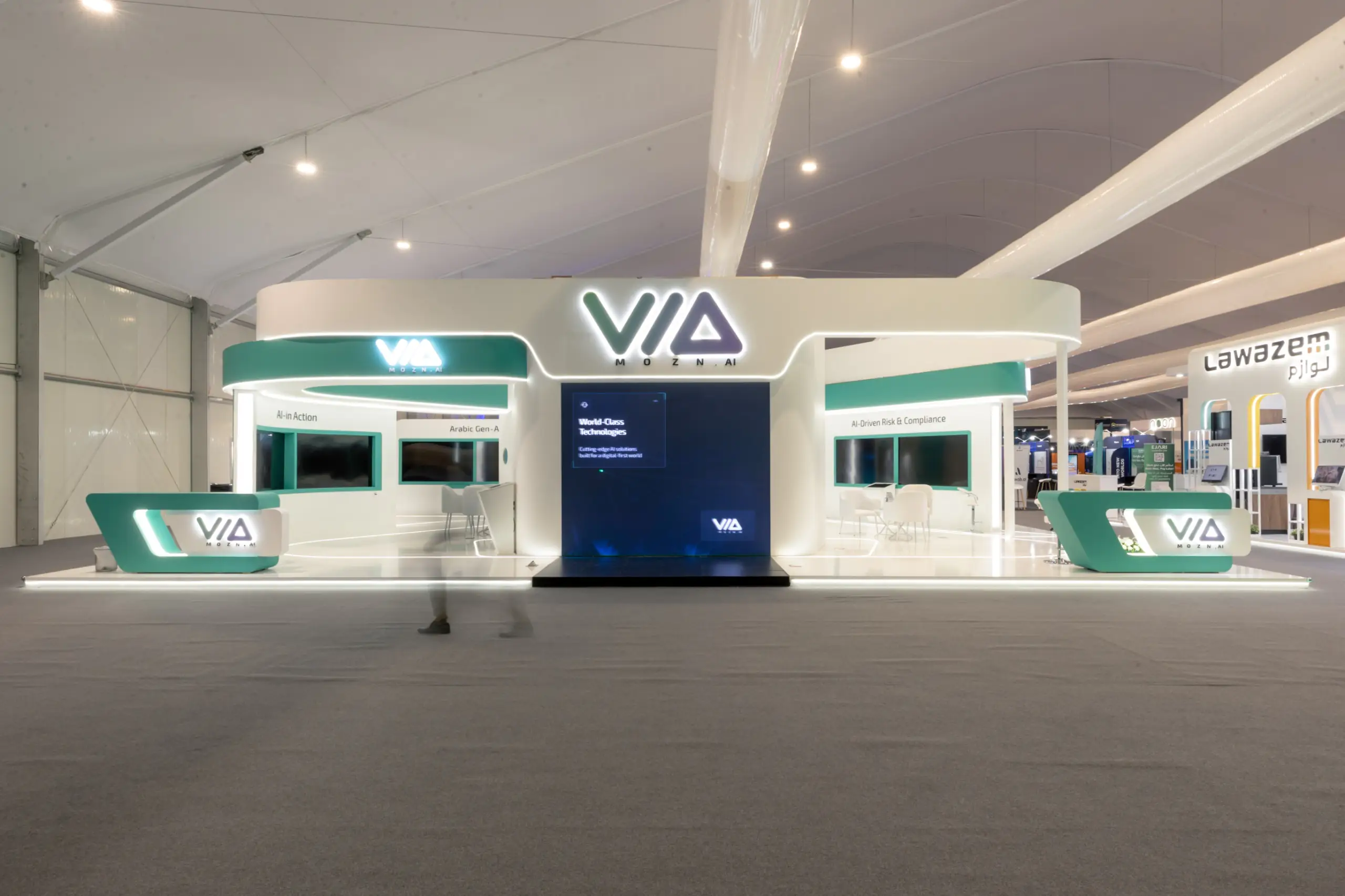 A sleek exhibition booth with a futuristic design, glowing white and green branding, and multiple interactive screens.