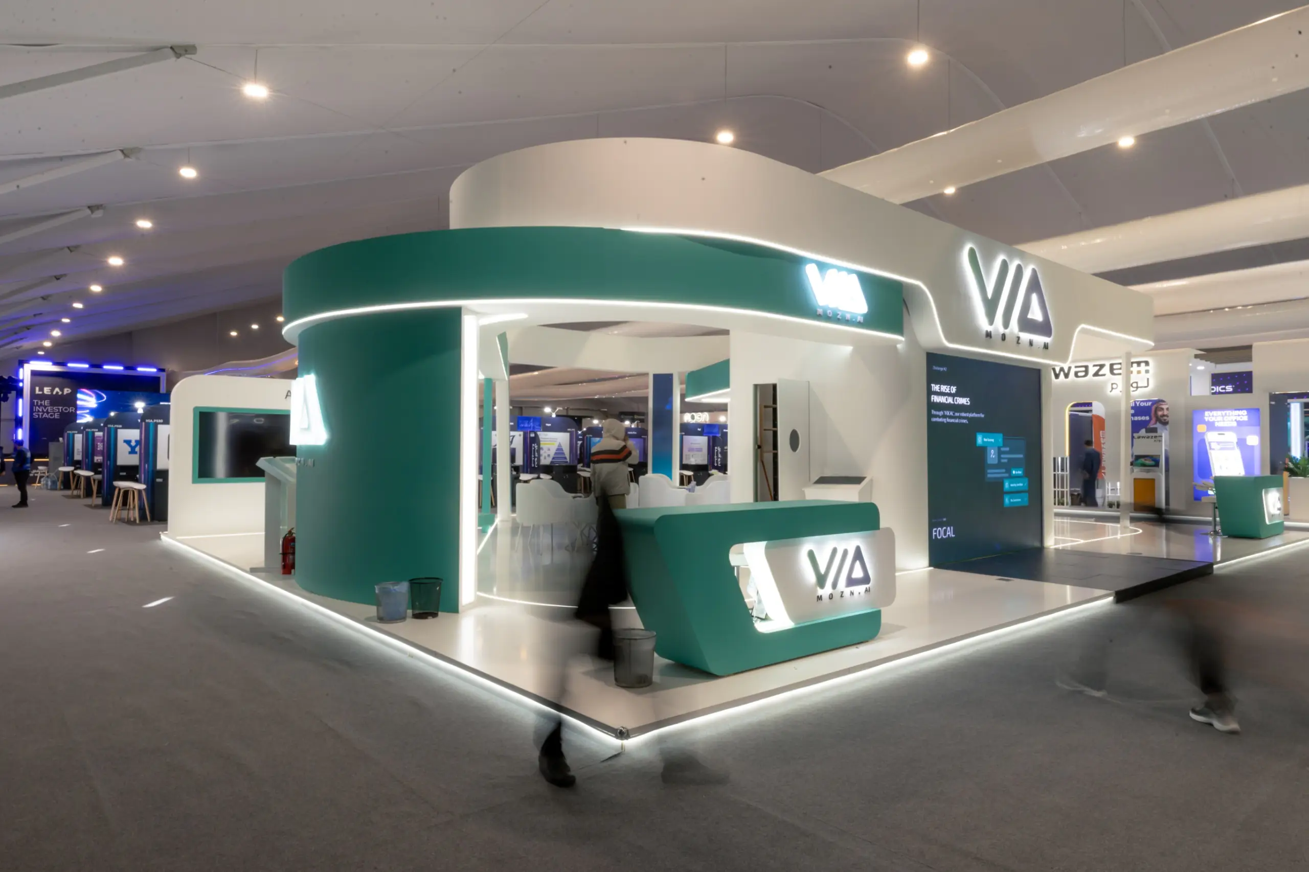 A high-tech trade show booth featuring digital screens, interactive stations, and a sleek, curved reception desk.