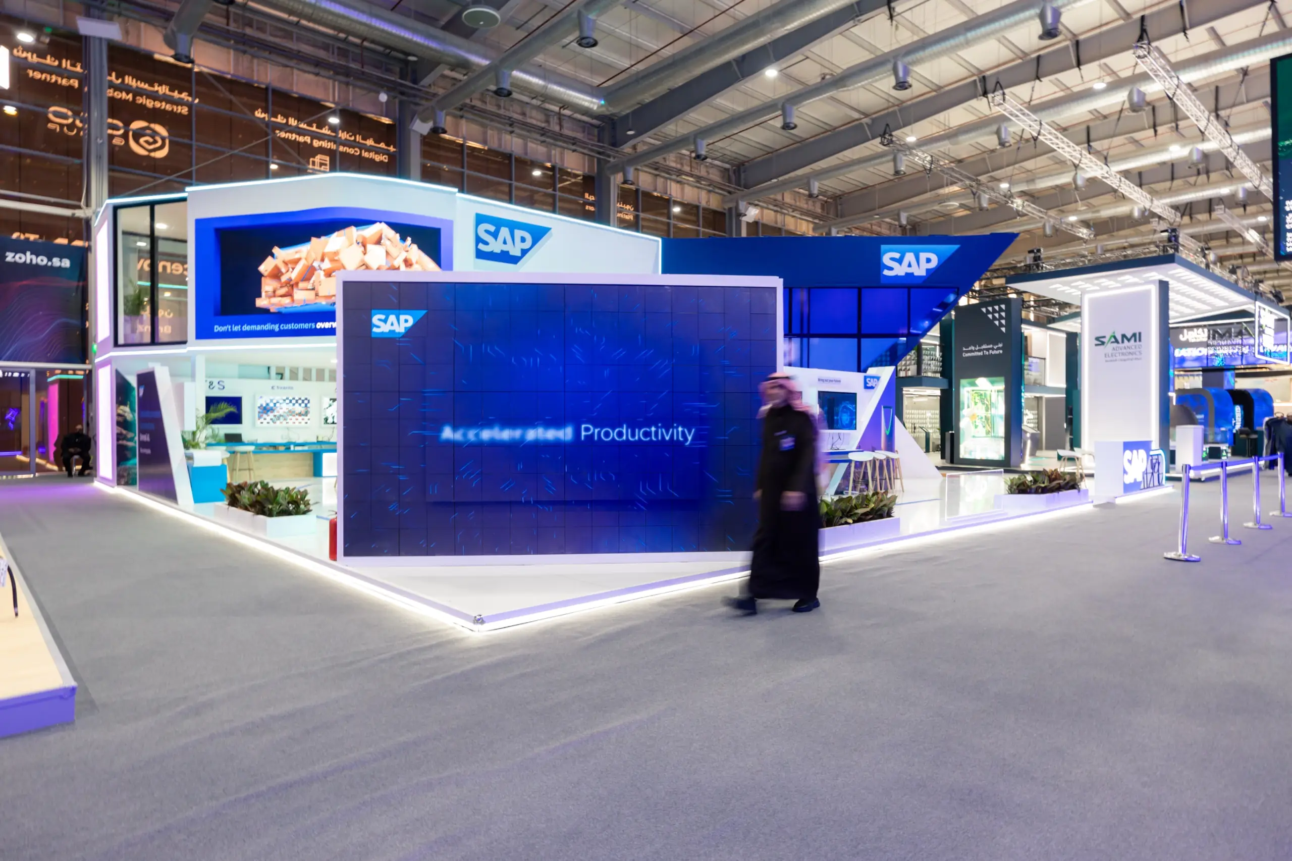 A futuristic SAP exhibition booth with large digital screens, blue lighting, and interactive displays showcasing productivity.