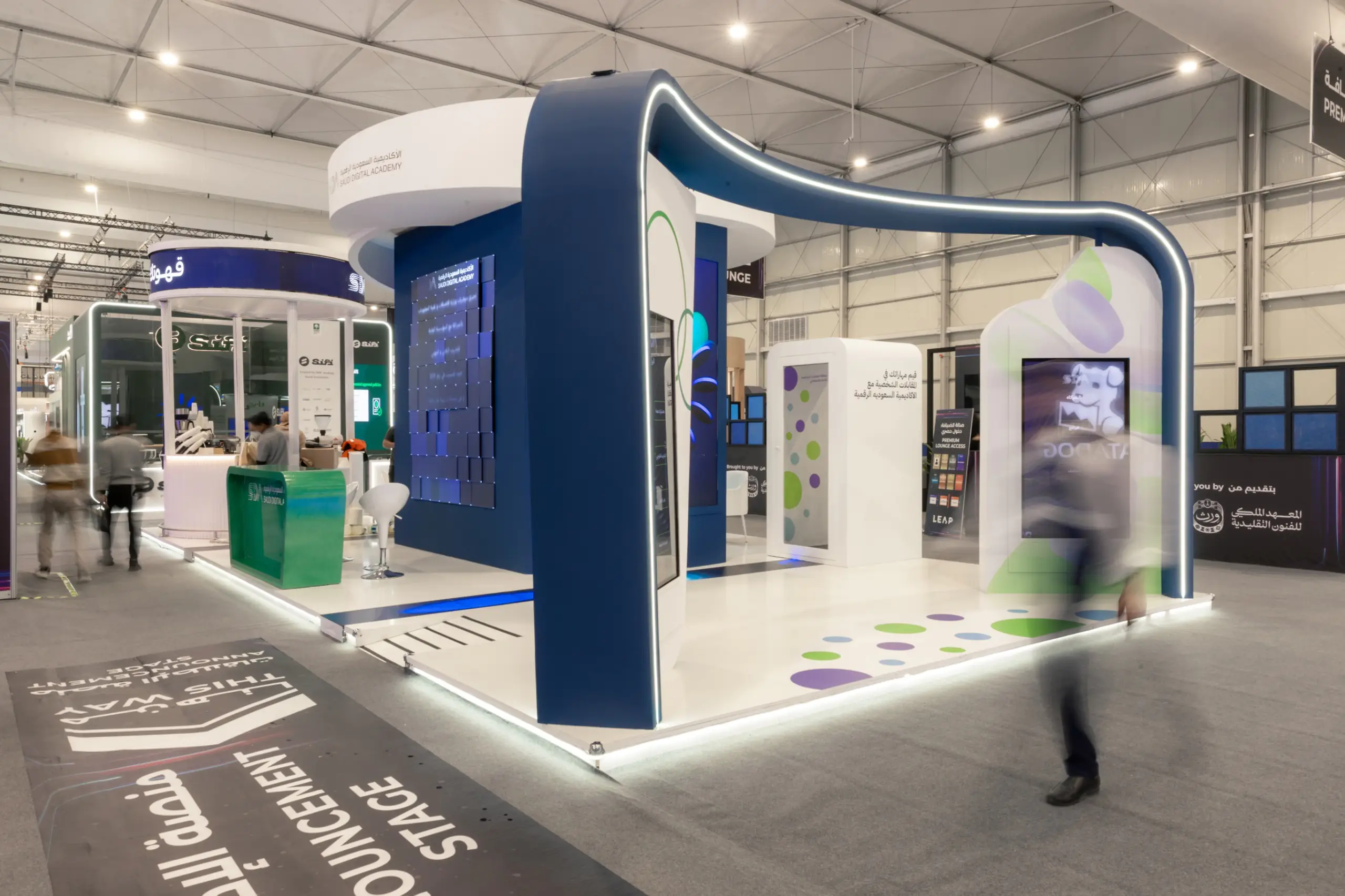 A modern trade show booth with blue and white structures, featuring digital panels and an engaging design.