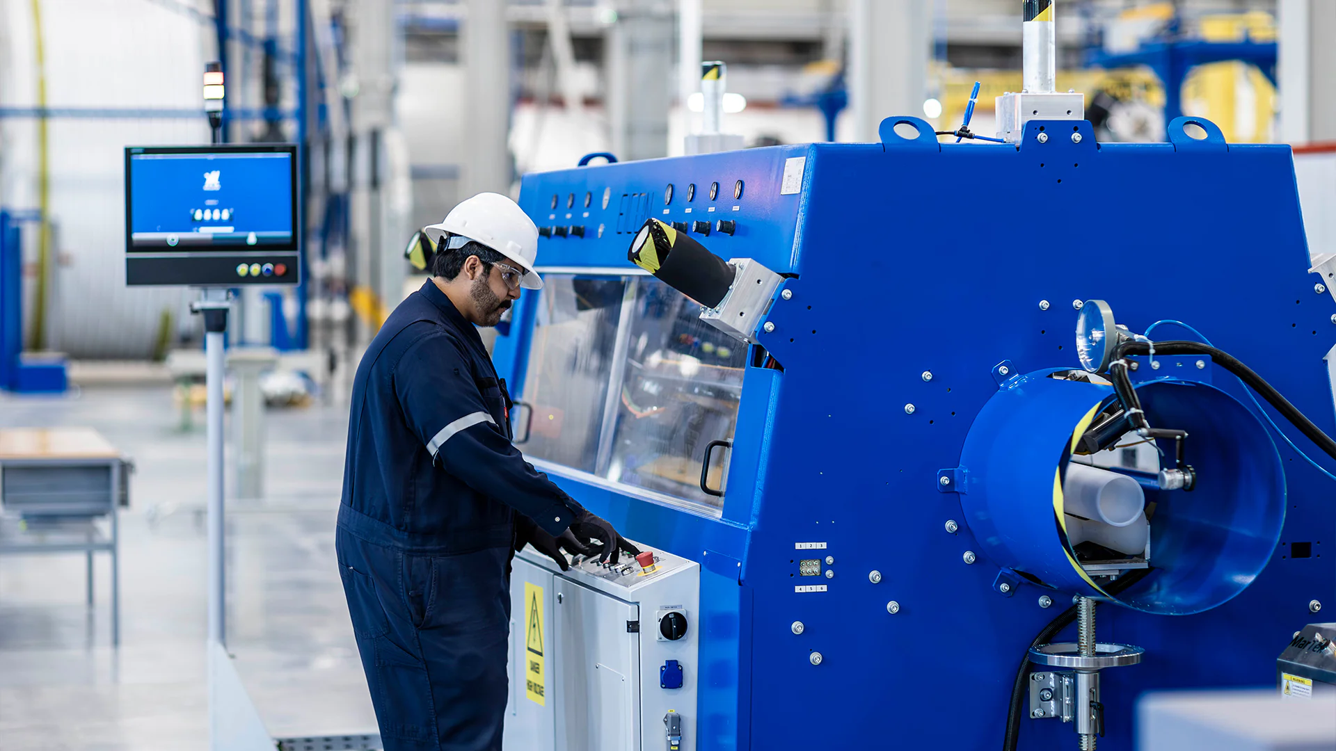 Technician in helmet and goggles operates a blue industrial machine via its control panel
