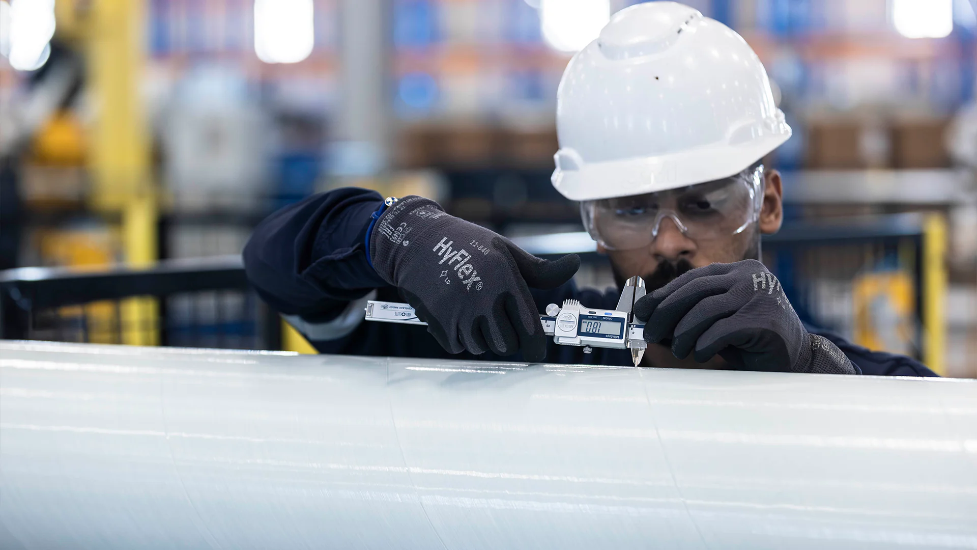 Close-up of a worker’s gloved hands measuring a metal piece with a digital caliper.