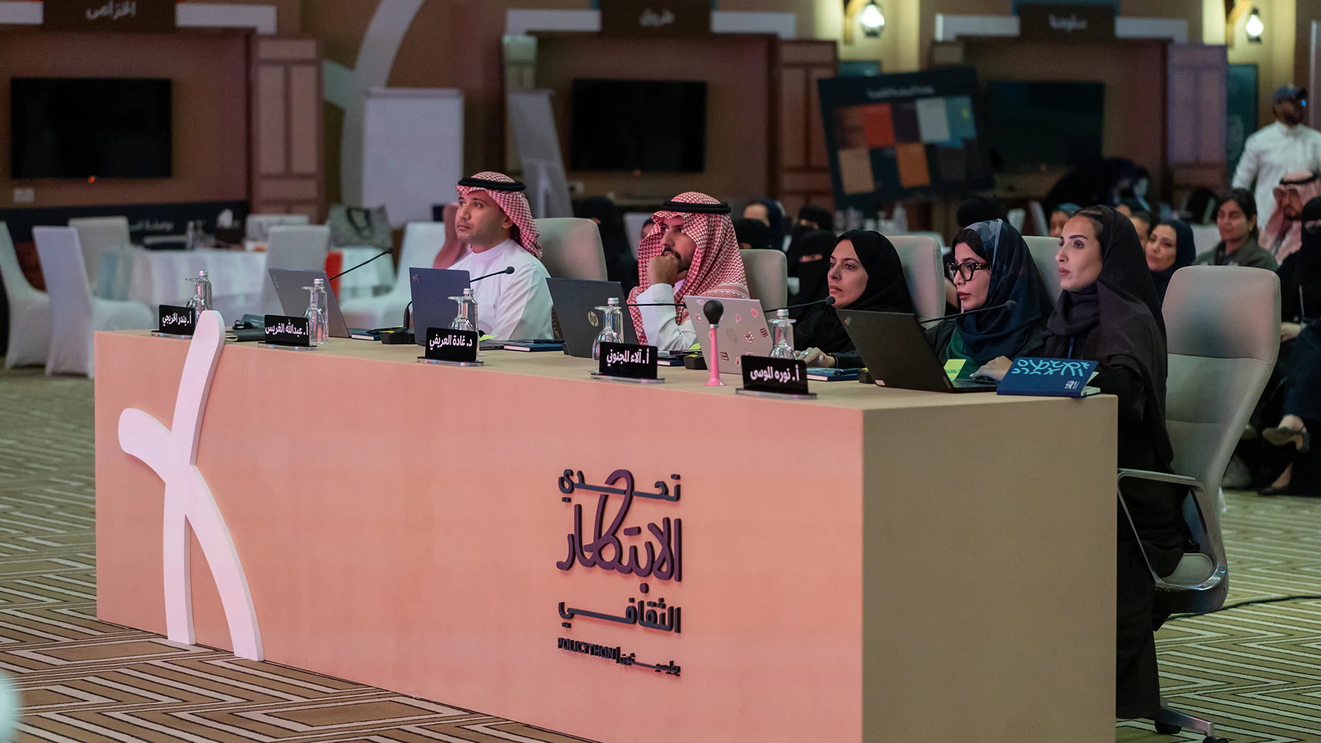 Judges at the Policython final event focused on participant presentations in a modern Saudi-themed setup.