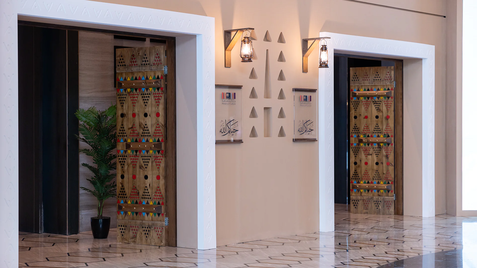 Close-up of traditional Najdi doors flanked by wall lanterns and Ministry of Culture branding.