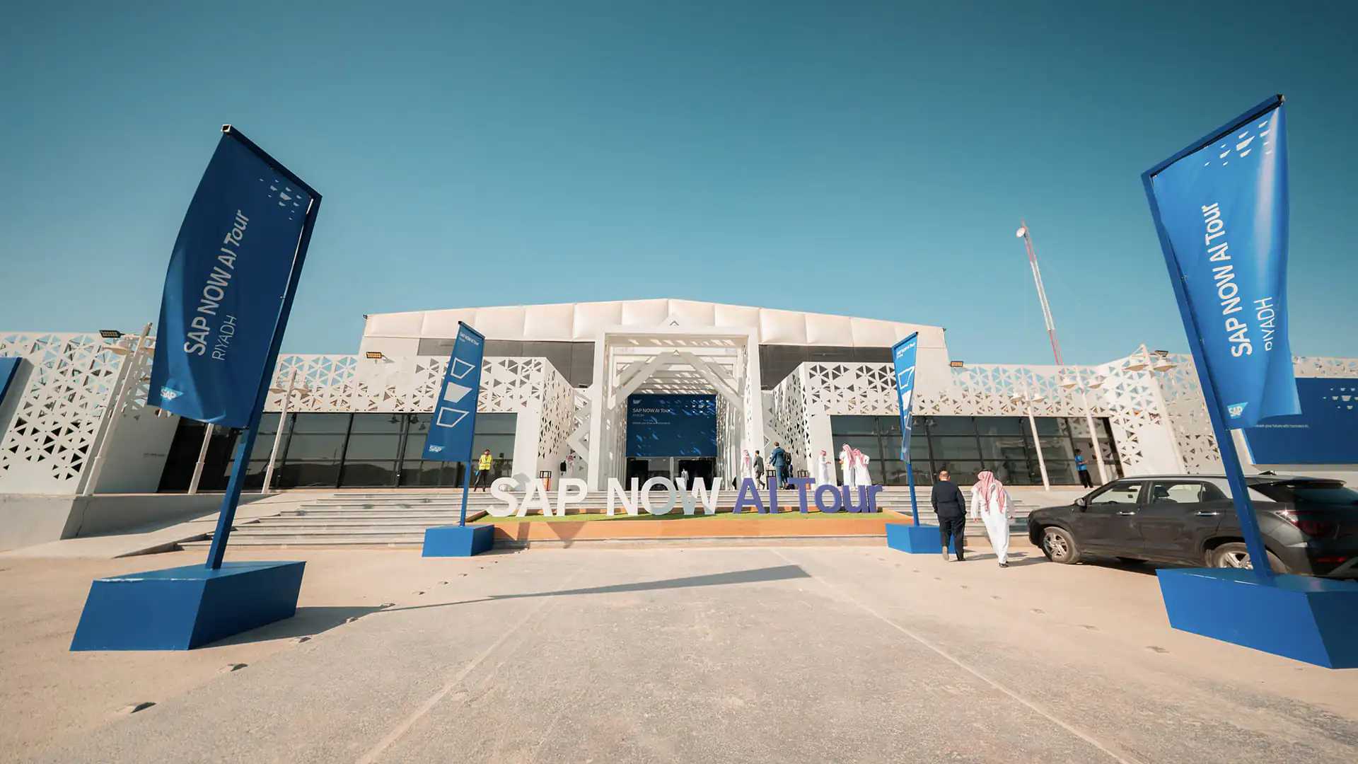 SAP NOW AI Tour Riyadh venue entrance with blue flags, signage, and attendees arriving.
