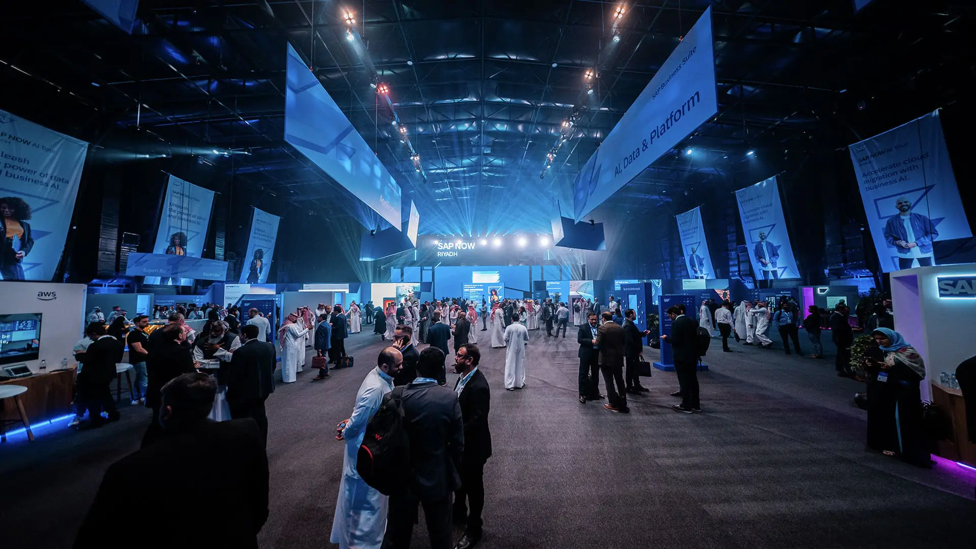 Large crowd networking across SAP NOW AI Tour zones under blue event lighting.