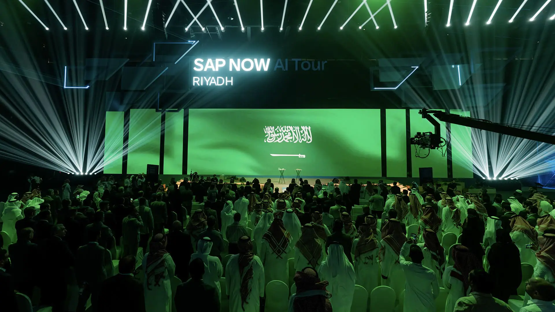 Audience stands as the Saudi flag appears onstage during SAP NOW AI Tour opening.