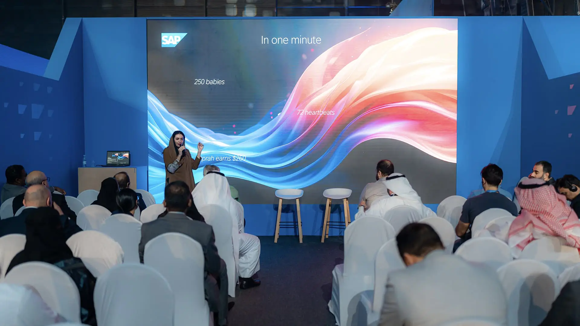 Speaker presents at a SAP NOW AI Tour breakout session with colorful screen graphics.