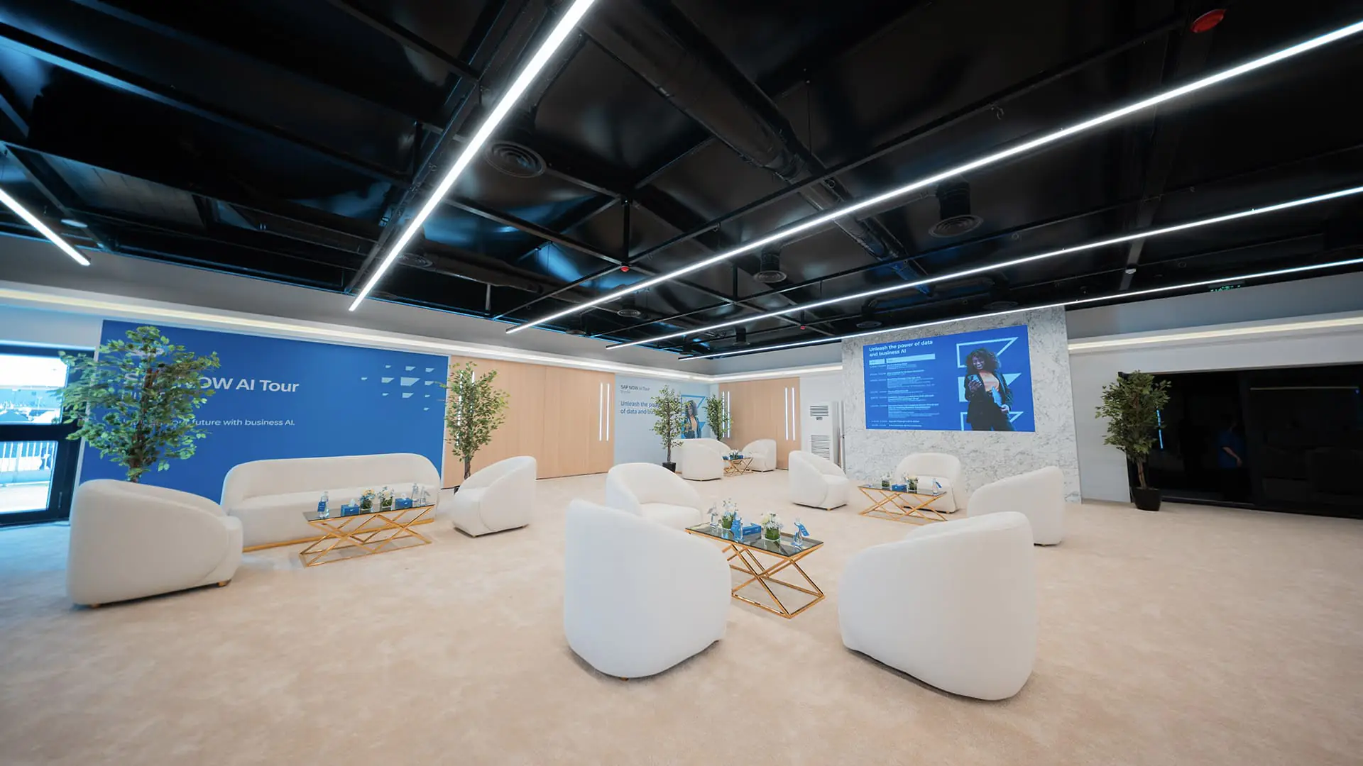 Bright VIP lounge with white chairs, SAP backdrop, and a large presentation screen.