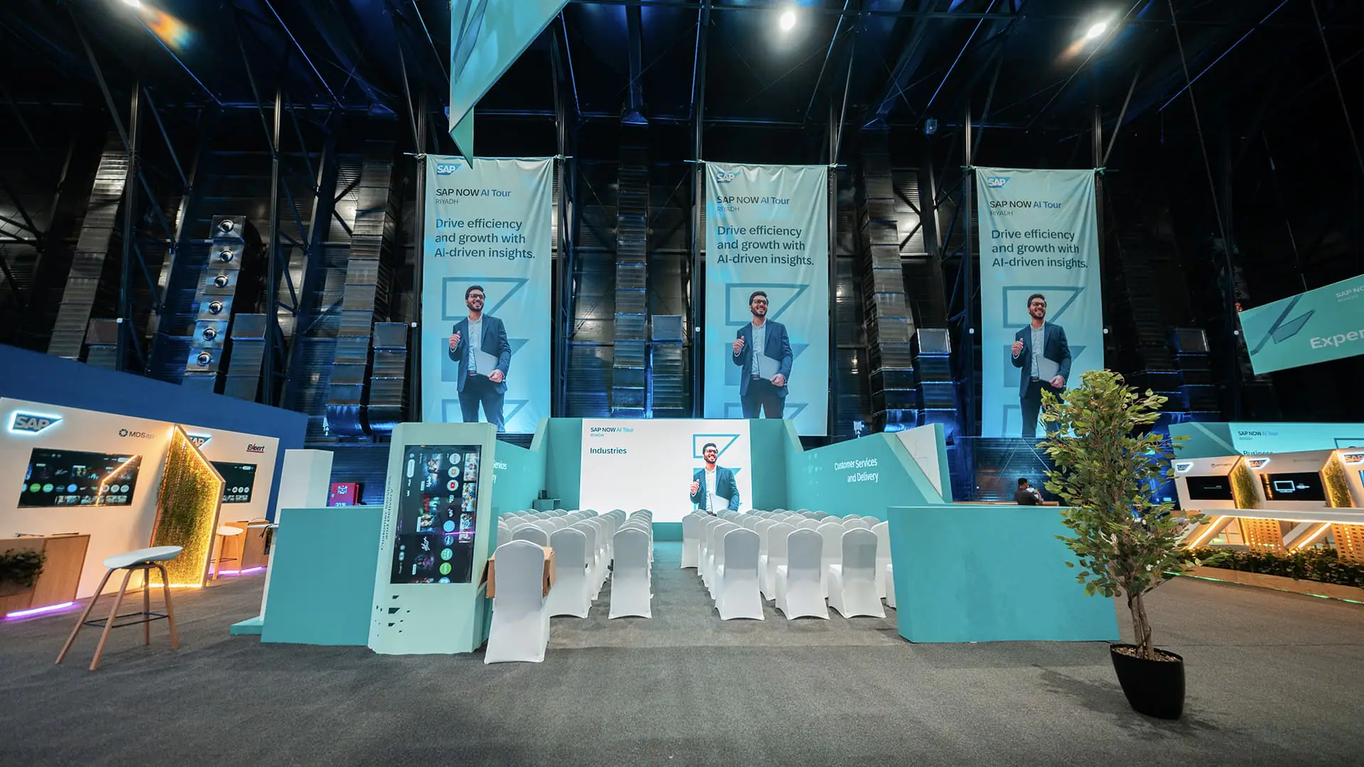 SAP NOW AI Tour theater setup with white chairs, large banners, and demo booths.