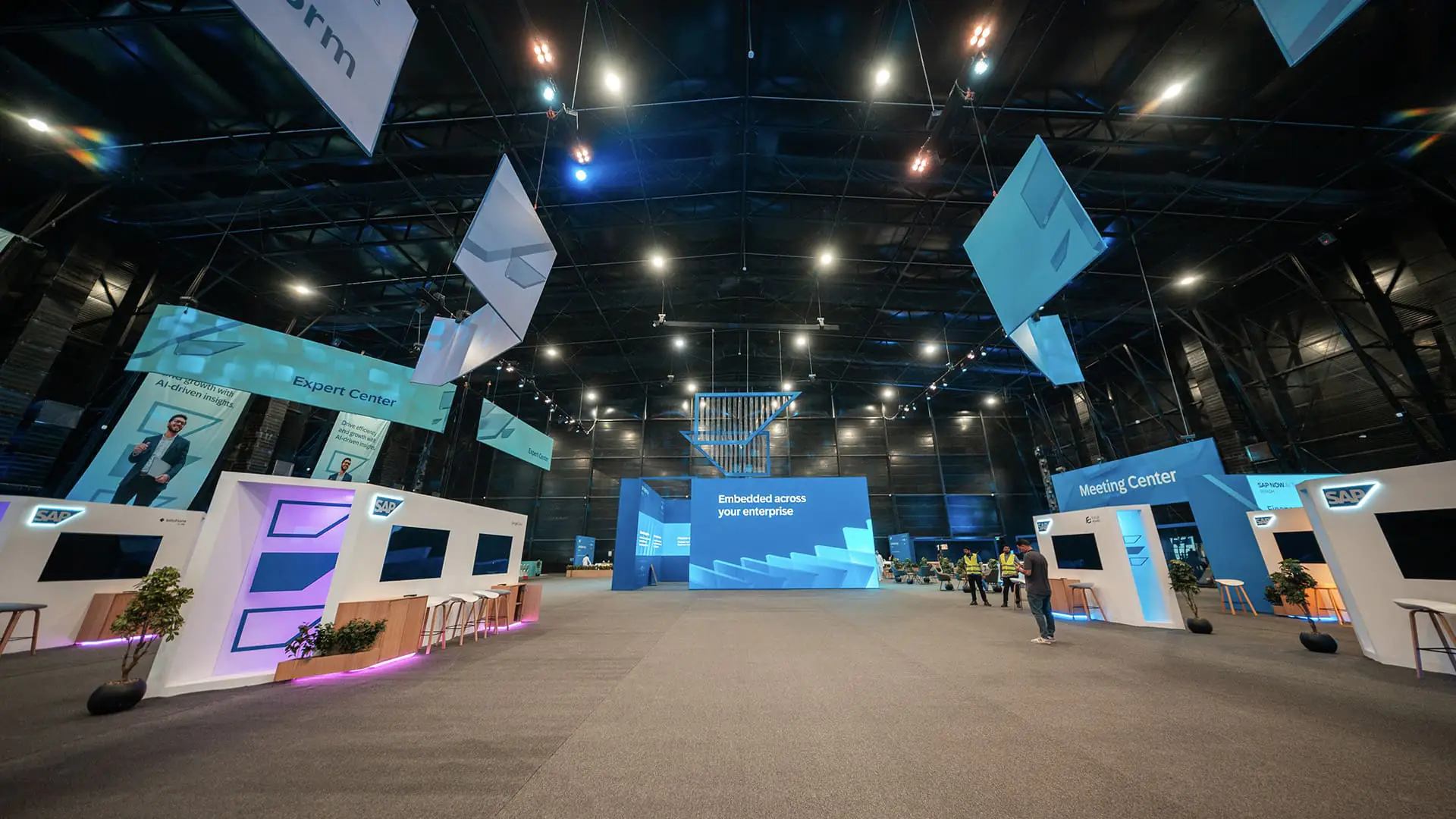 Spacious SAP NOW AI Tour exhibition hall with demo pods and overhead banners.