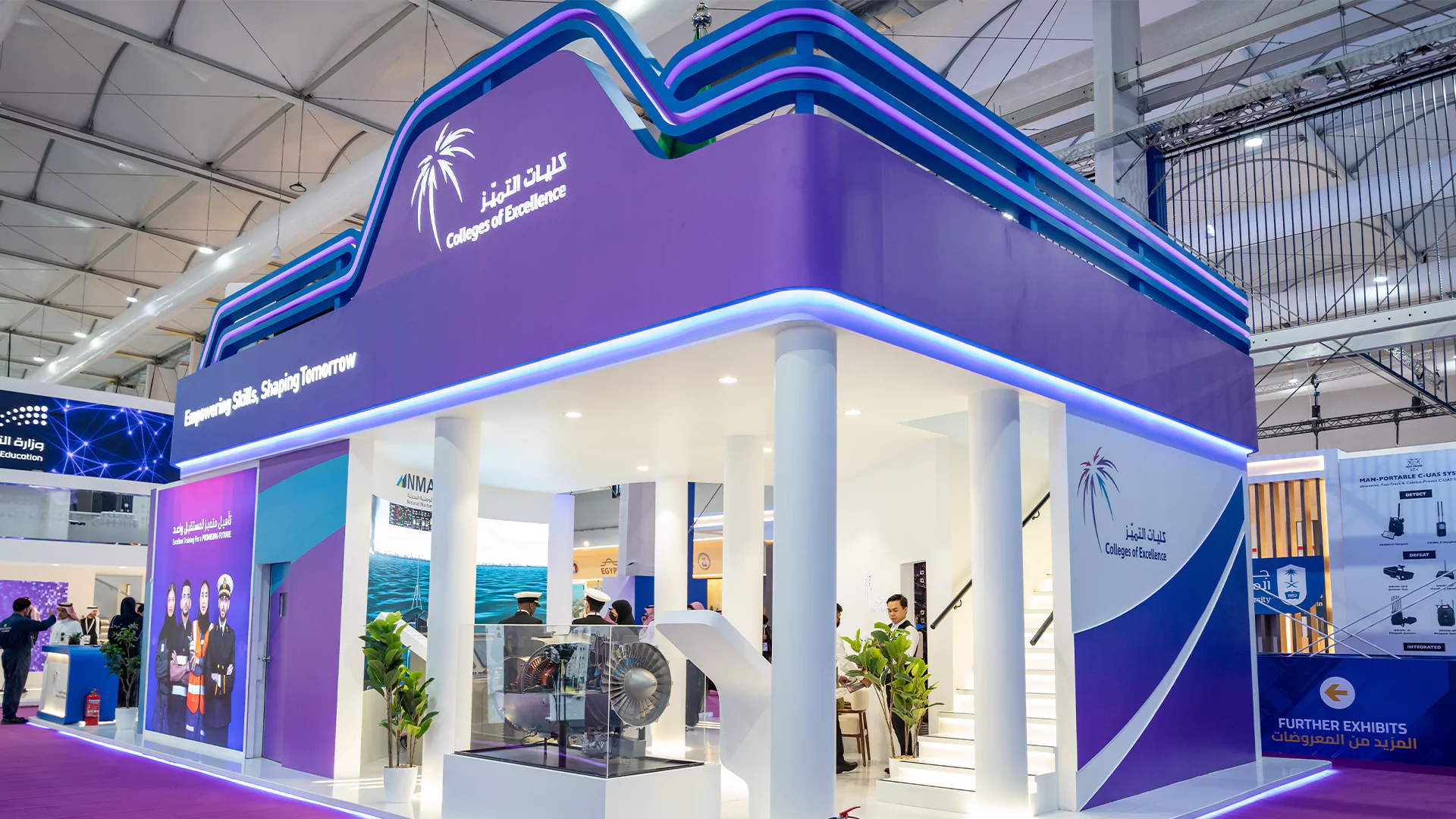 Exterior corner of the two-story College of Excellence booth showing aircraft engine display and stairs, WDS 2026.