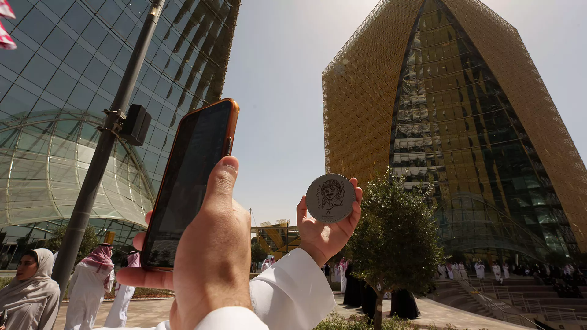 Visitor photographing engraved souvenir coin during Eid activation at Digital City