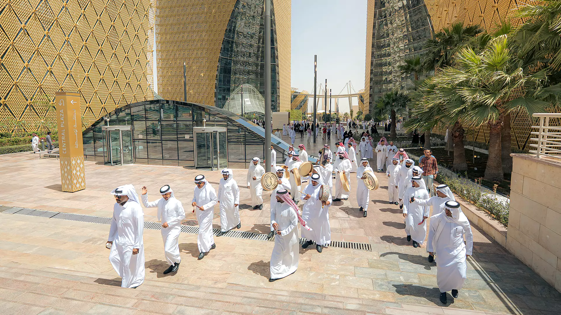 Cultural parade with drummers and participants walking through Digital City plaza