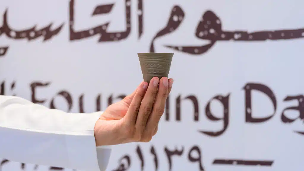 Close-up of a hand holding a traditional patterned Saudi coffee cup for Founding Day celebrations